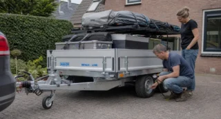 Man controleert bandenspanning van beladen aanhanger voor vertrek, vrouw staat ernaast.