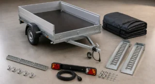 Open aanhangwagen met praktische accessoires: spanbanden, laadrampen, achterlichten, bevestigingsmateriaal en beschermhoes.